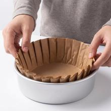 Hands placing a pleated kraft Basque cheesecake liner into a round cake tin