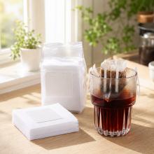 Hanging drip coffee filter bag brewing over a glass cup beside a stack of filter bags
